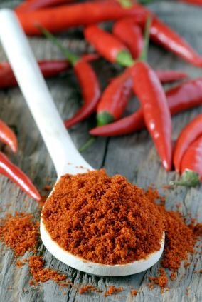 close up of spoon heaped with chilli powder with red chillies in background