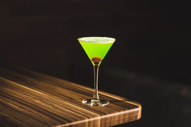 zielony drink na cienkiej nóżce na drewniany blacie na czarnym tle