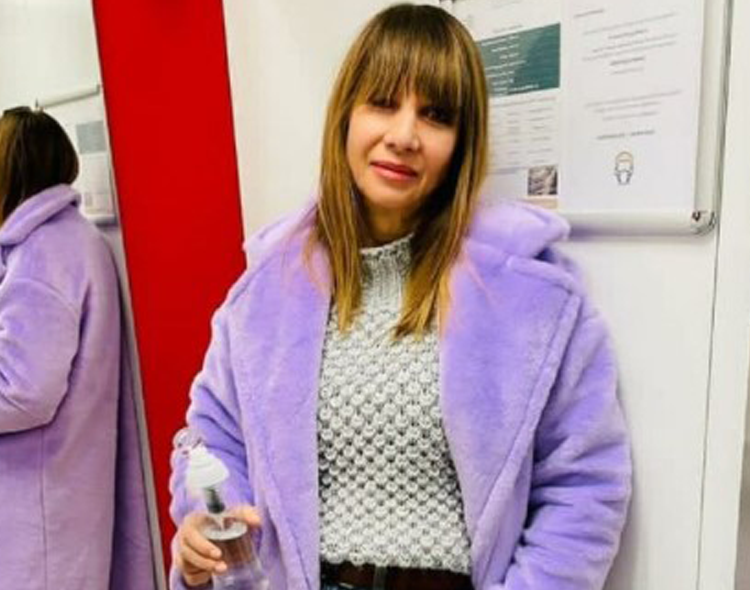 Grażyna Wolszczak w fioletowym płaszczu pozuje na tle białej ściany w dżinsach
