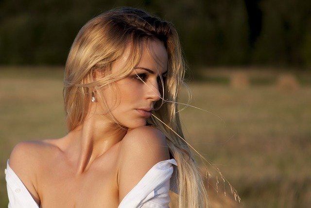 blondynka z rozwianymi na wietrze włosami w białej bluzce z dużym dekoltem na tle pola
