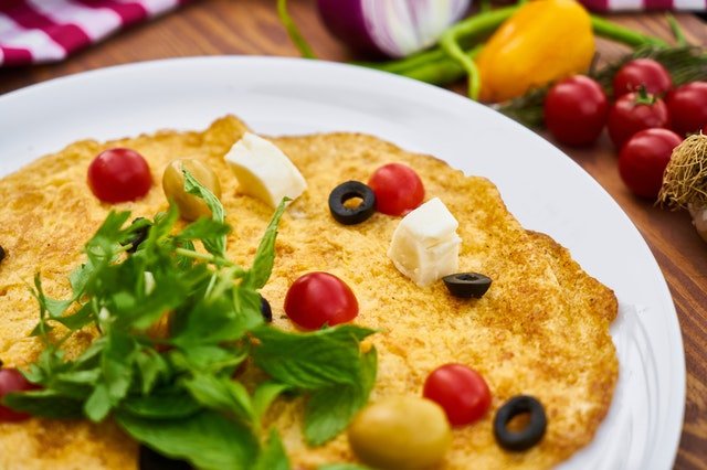 omlet na białym talerzu z sałatą, oliwkami i serkiem feta pokrojonym w kostkę
