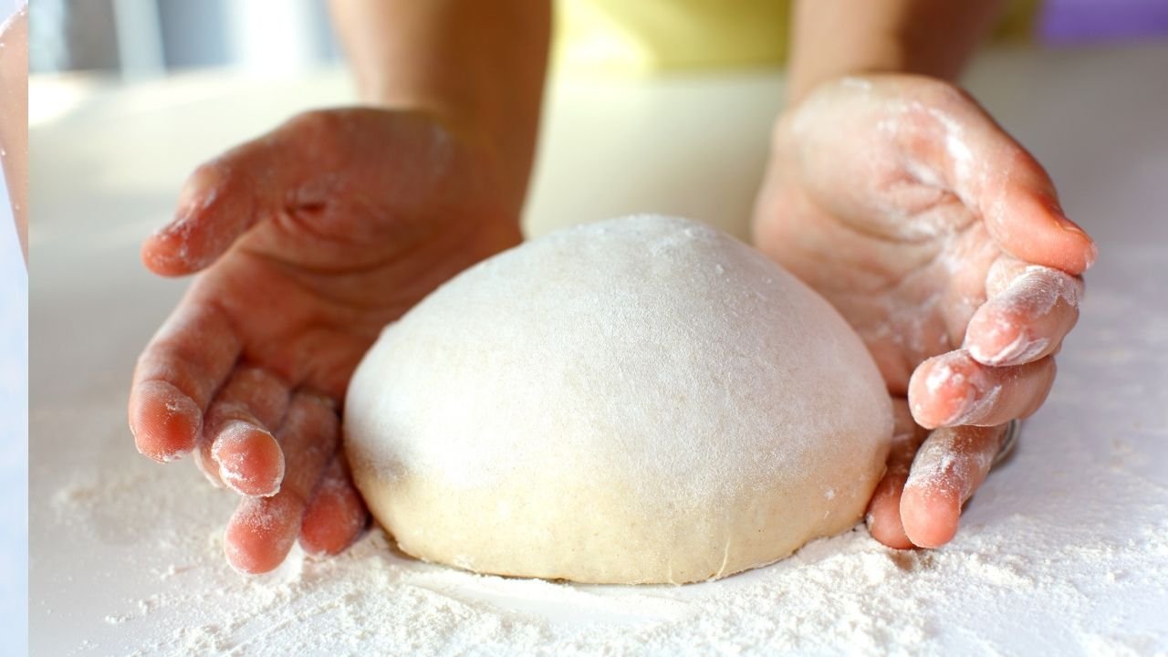ciasto do chleba położone na desce a obok ręce