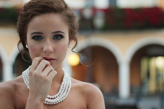 brunetka w spiętych włosach i perłach na szyi na tle starego budynku 