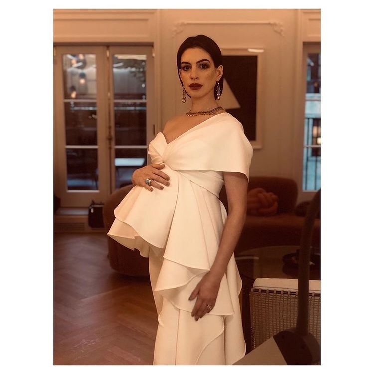 Anne Hathaway w kremowej sukni trzyma się za ciążowy brzuszek