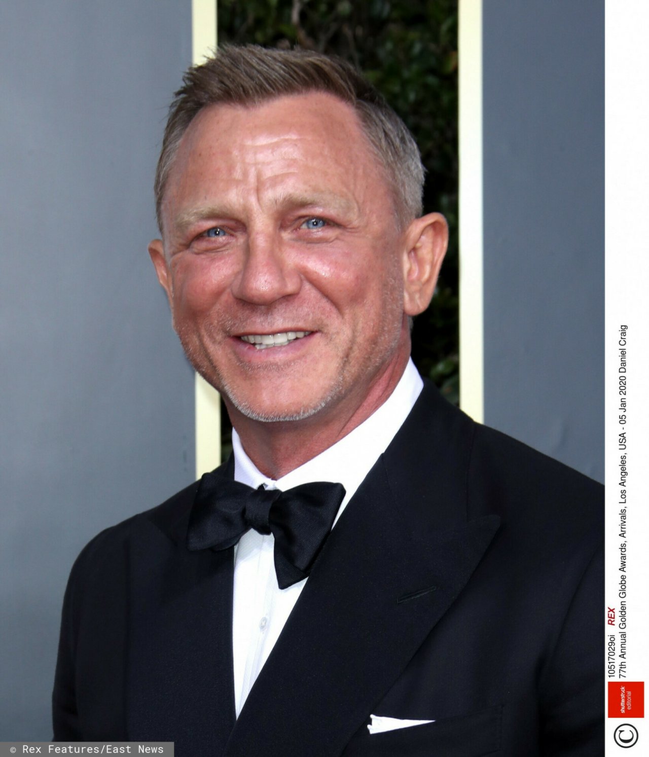 Daniel Craig w czarnym garniturze uśmiecha się szeroko 