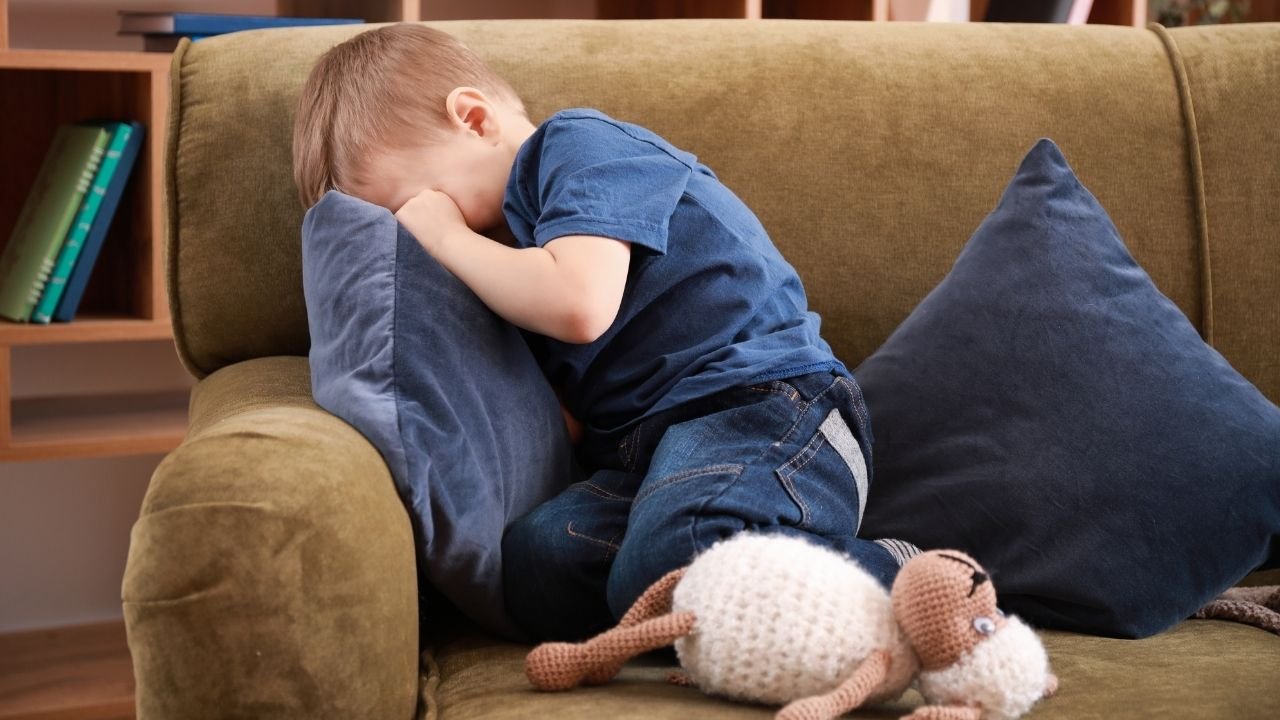 Mały chłopiec siedzi na kanapie i płacze w poduszkę