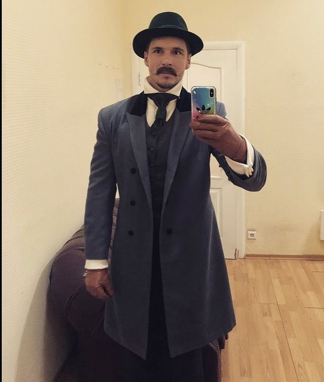 Mikołaj Roznerski w eleganckim stroju, cylindrze i z wąsem robi sobie selfie 