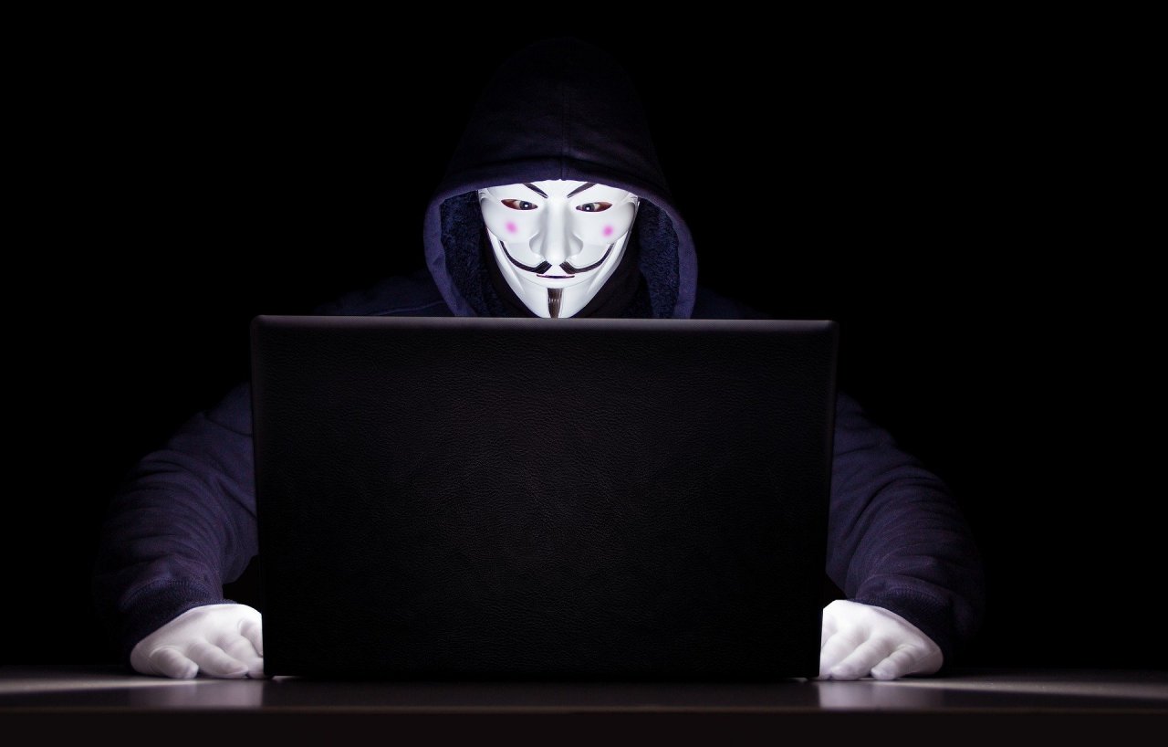 Haker z Anonymous siedzi przed laptopem