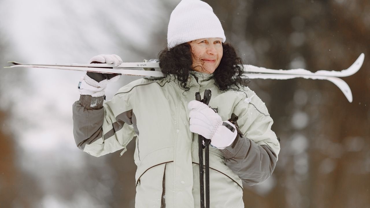 Kobieta w kurtce narciarskiej z nartami w ręce
