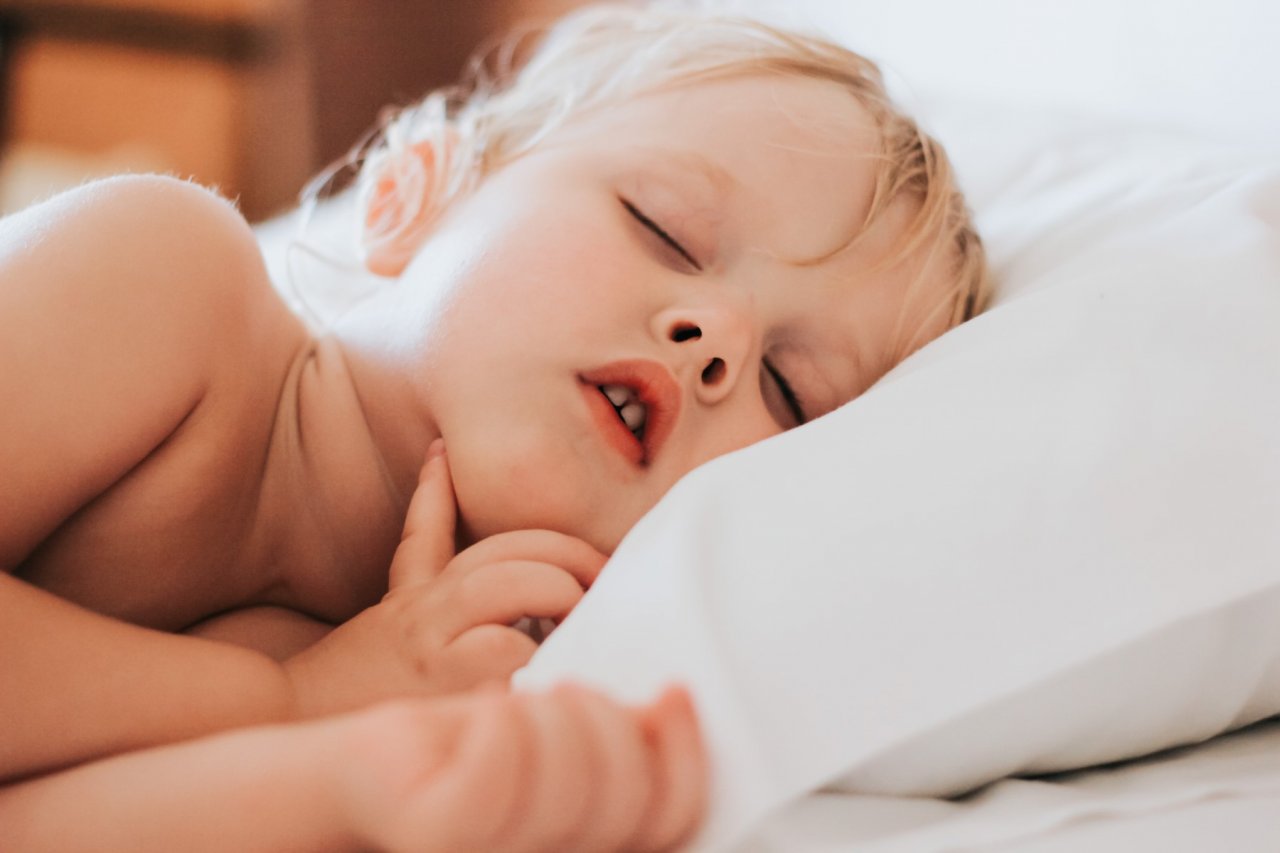 Małe dziecko o blond włoskach słodko śpi tuląc się do białej poduszki