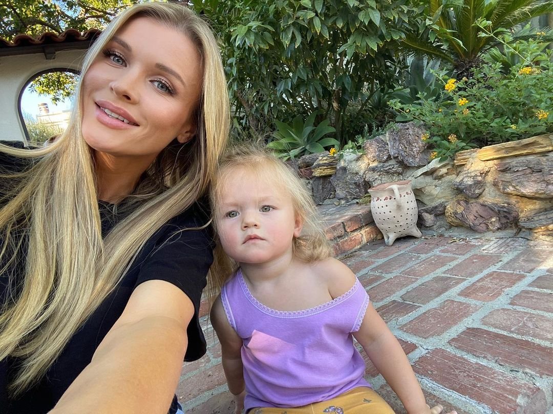 Joanna Krupa w czarnej bluzce i rozpuszczonych włosach siedzi obok małej Ashy w fiolecie