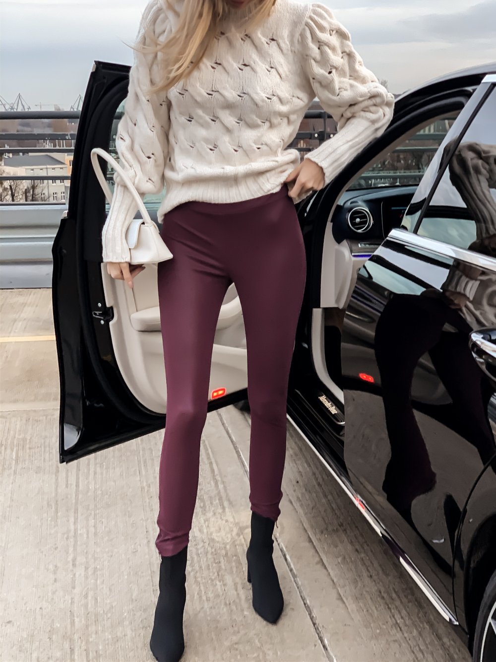 Kobieta ubrana w eleganckie leginsy i casualowy sweter stoi przy czarnym samochodzie
