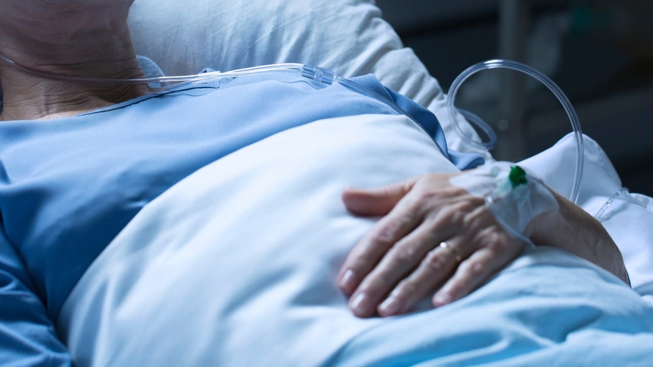 kobieta w niebieskiej piżamie leży w szpitalnym łóżku przykryta jasną kołdrą