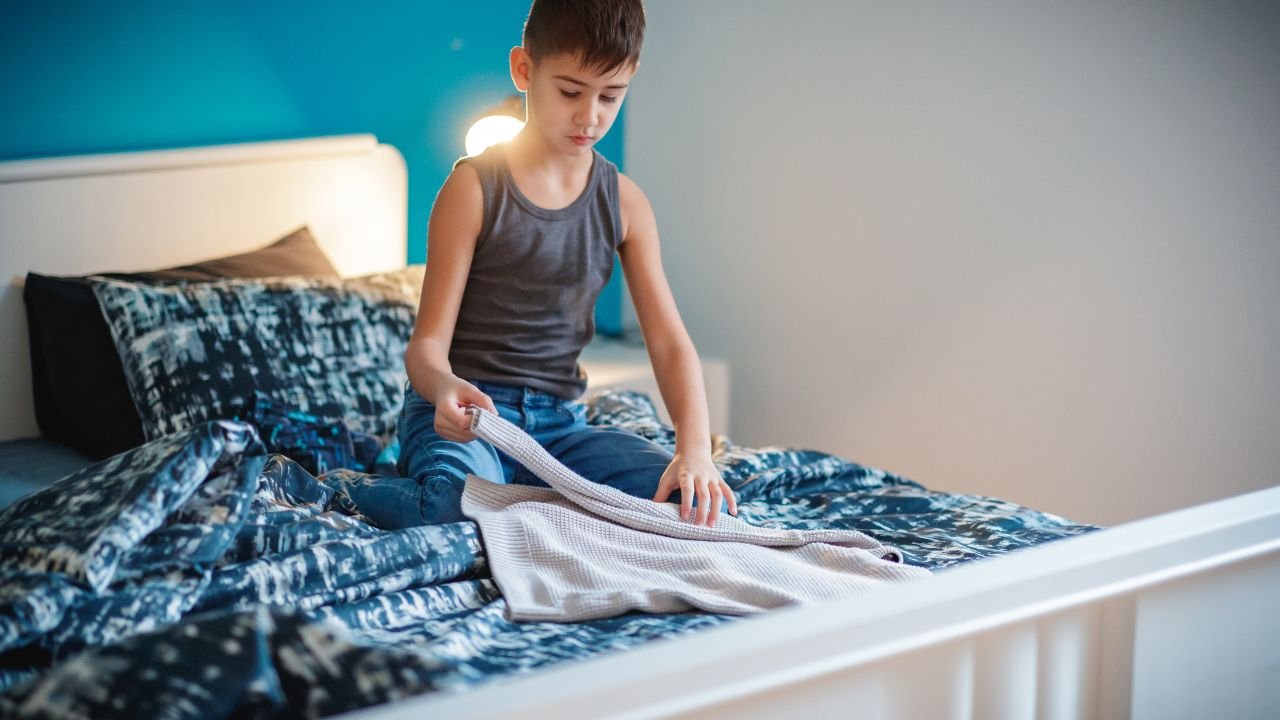 chłopiec składa ubrania na łóżku
