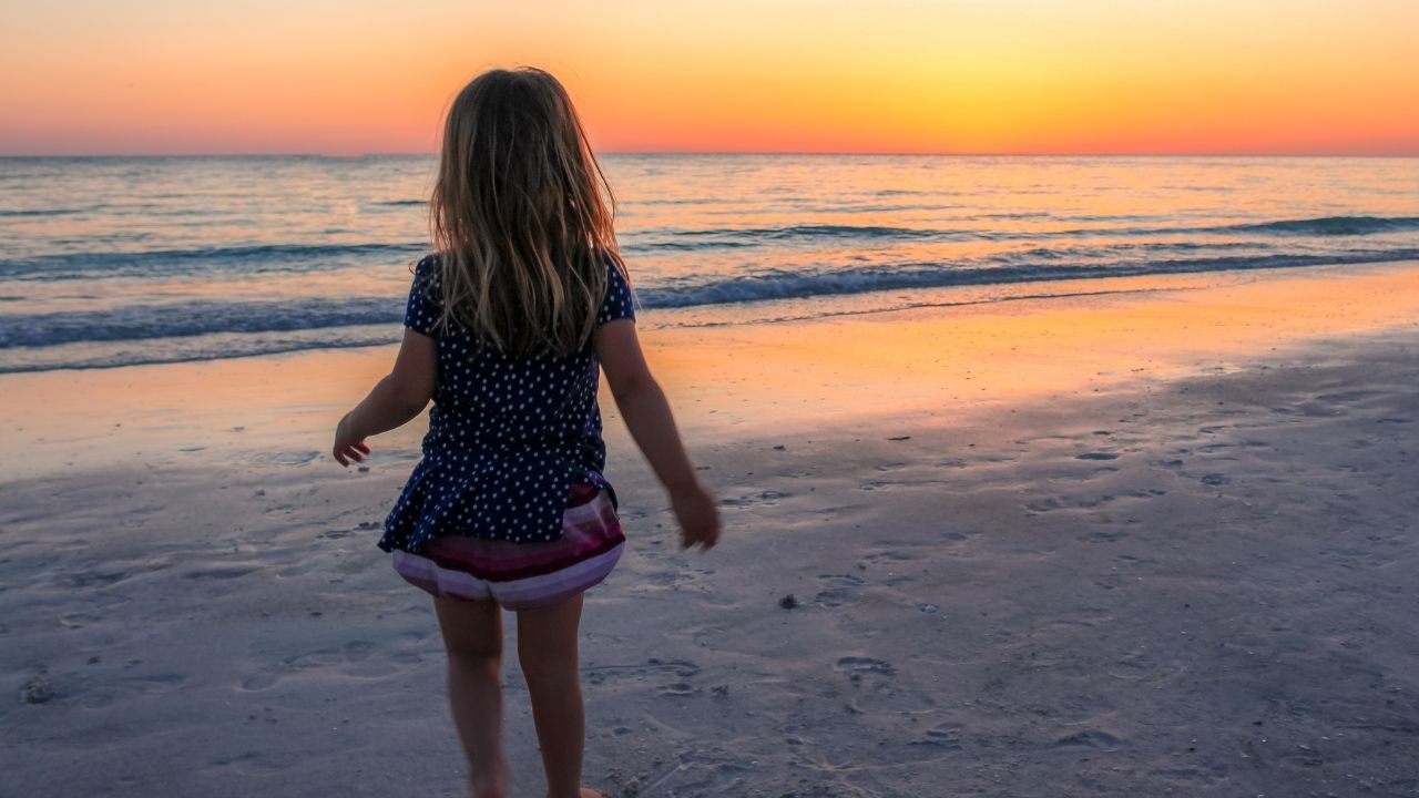 Mała dziewczynka stoi tyłem na tle zachodu słońca nad morzem