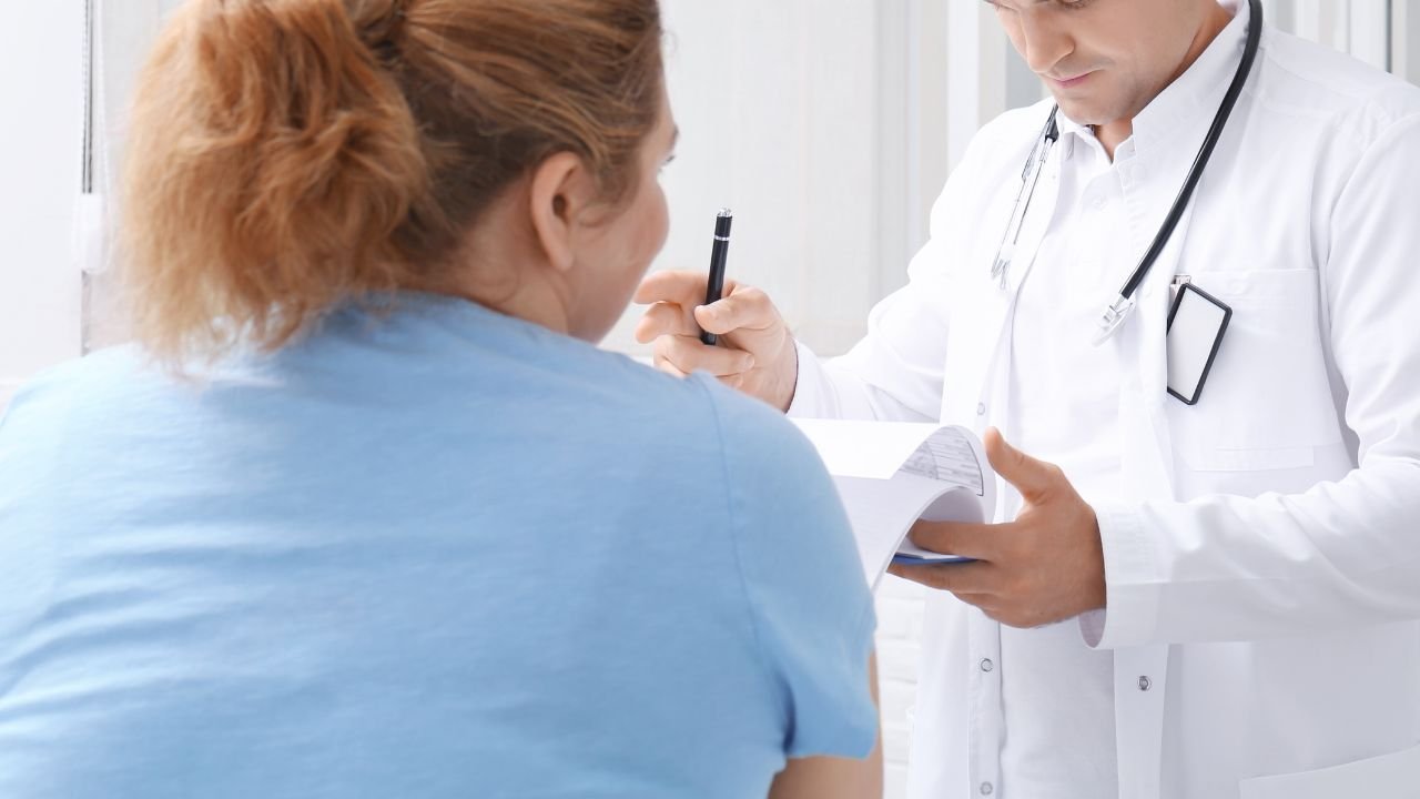 kobieta w spiętych włosach i niebieskiej koszulce siedzi przed ubranym na biało lekarzem 