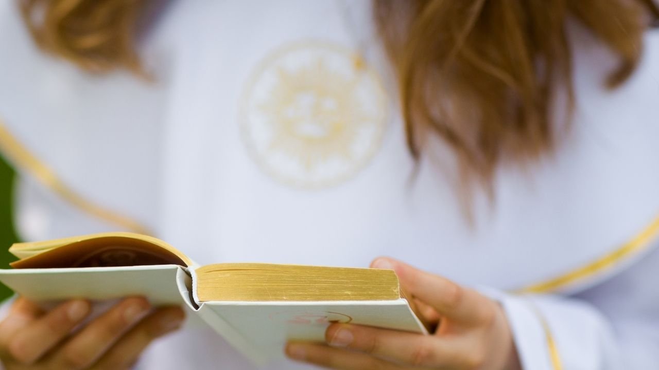 dziewczynka w białej albie trzyma w dłoniach białą książeczkę