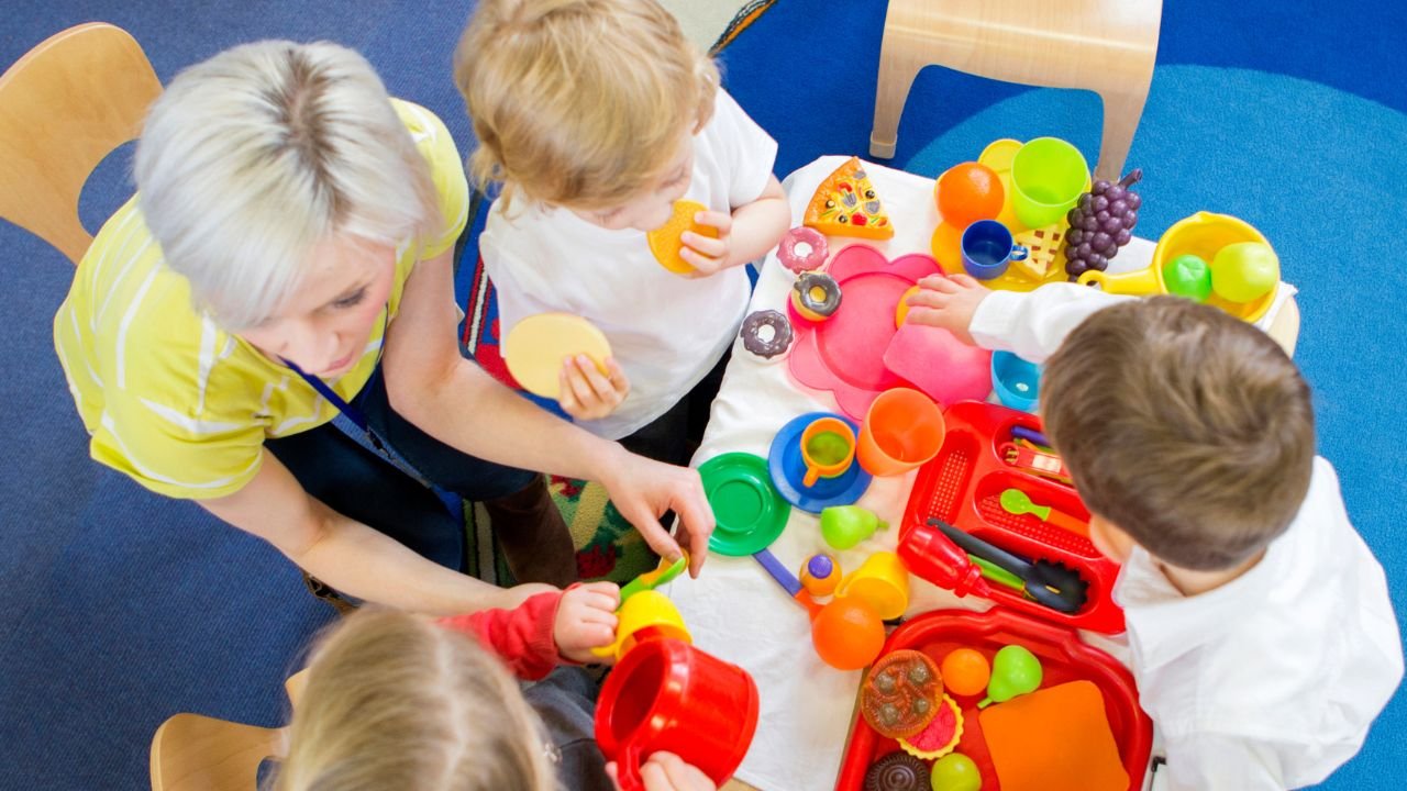 troje dzieci siedzi przy małym stoliku z plastikowymi zabawkami