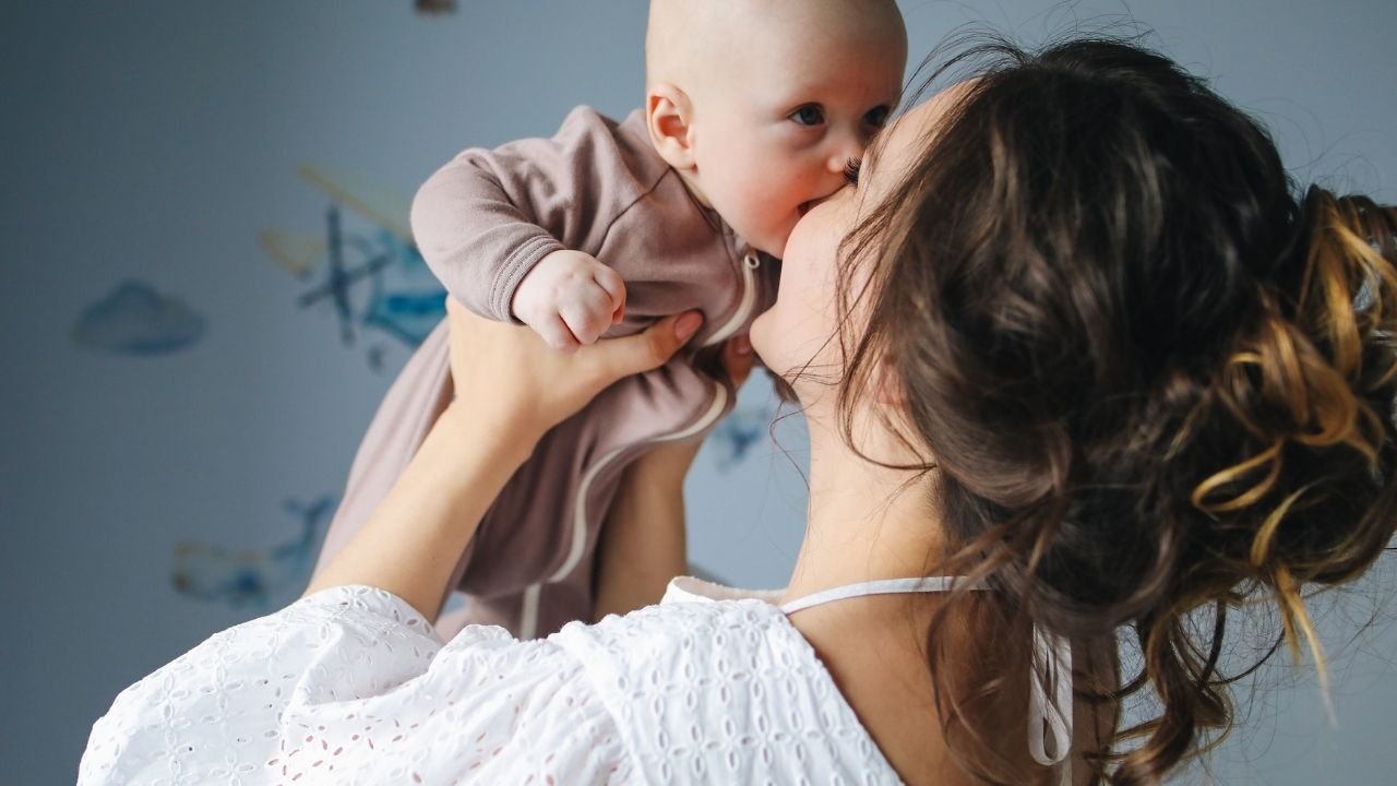 kobieta trzyma niemowlę na rękach i je całuje w usta