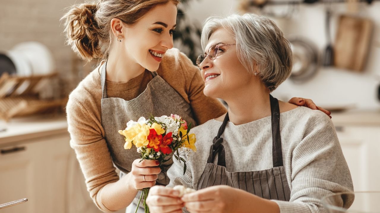 Młoda kobieta w fartuchu kuchennym daje bukiet kwiatów babci w okularach