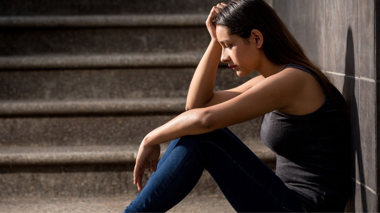Smutna dziewczyna siedzi pod ścianą