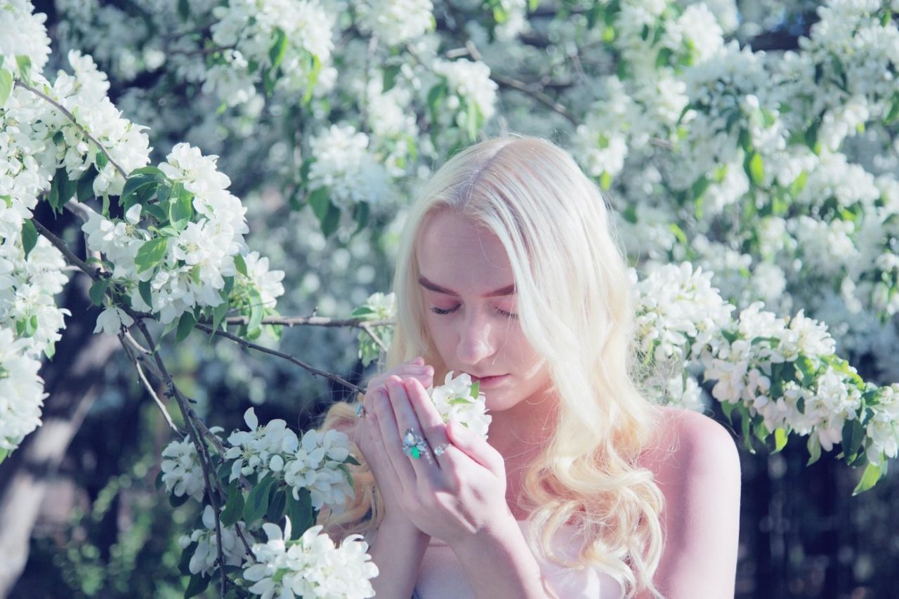 Kobieta jasne blond włosy na tle kwitnącego drzewa wącha kwiaty