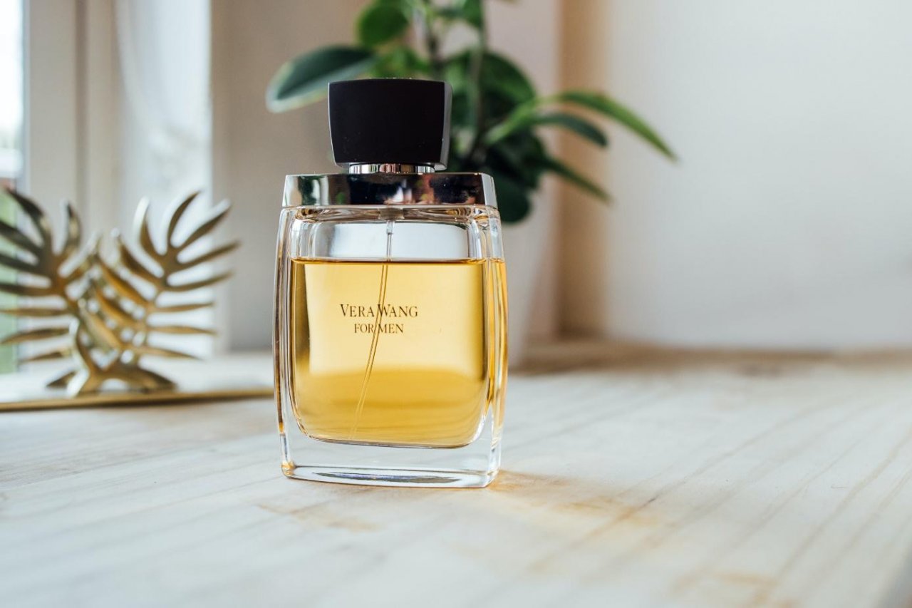 Buteleczka złotych damskich perfum na drewnianym blacie na tle okna