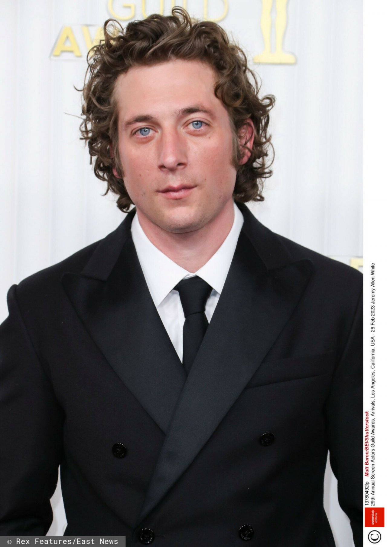 Jeremy Allen White w czarnej marynarce, białej koszuli i czarnym krawacie pozujący na ściance