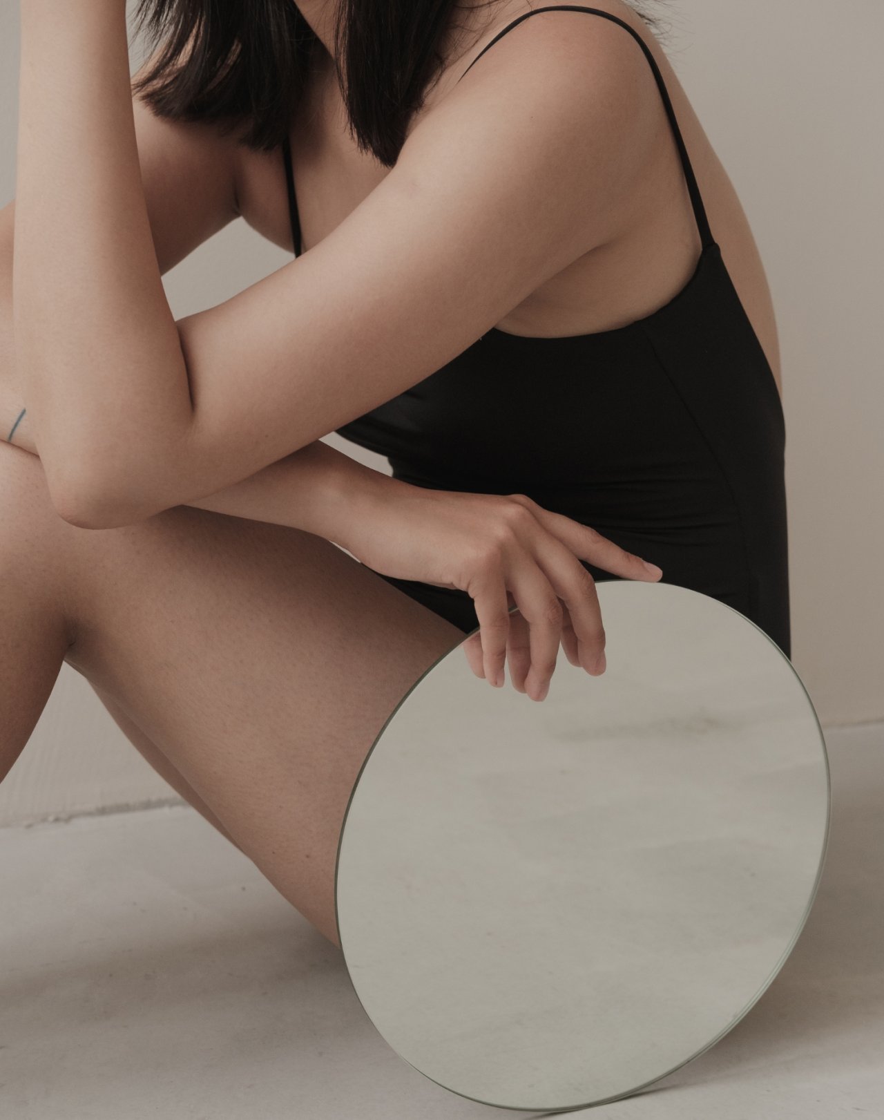 Kobieta w czarnym body zasłaniająca swoje ciało okrągłym lustrem