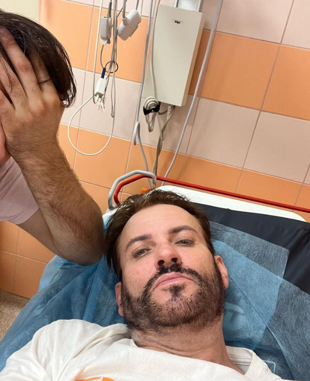 Zbliżenie na twarz Gabriela Seweryna na szpitalnym łóżku a obok niego siedzi mężczyzna