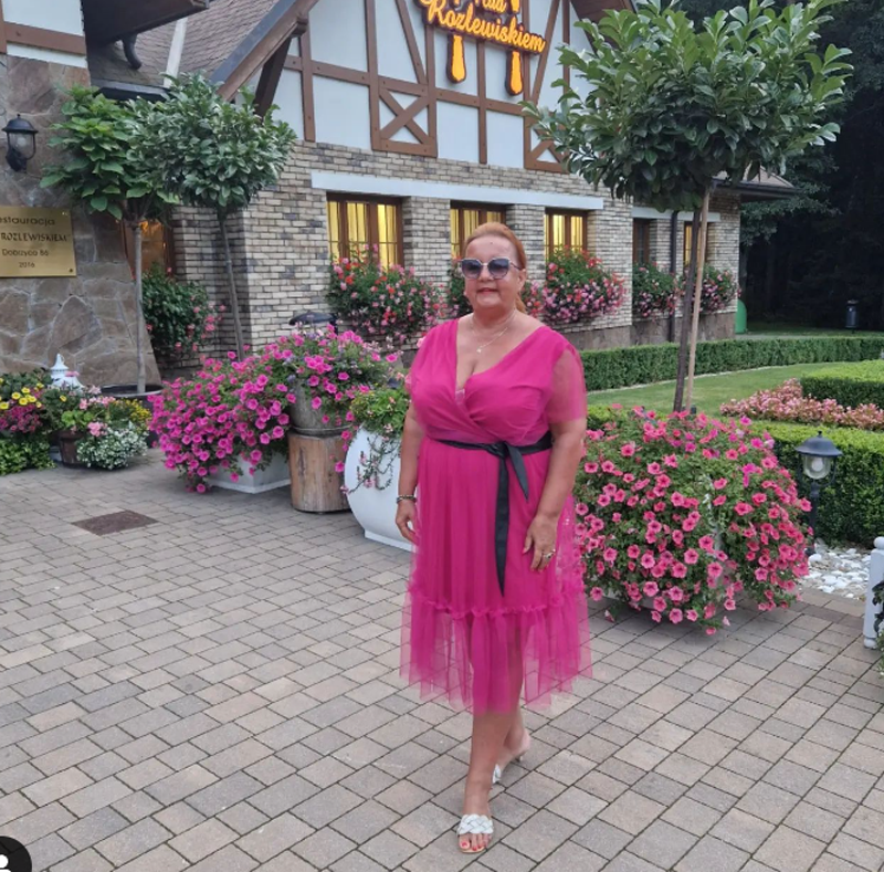 Iza Zeiske w różowej sukience stoi na chodniku przed kwiatami 