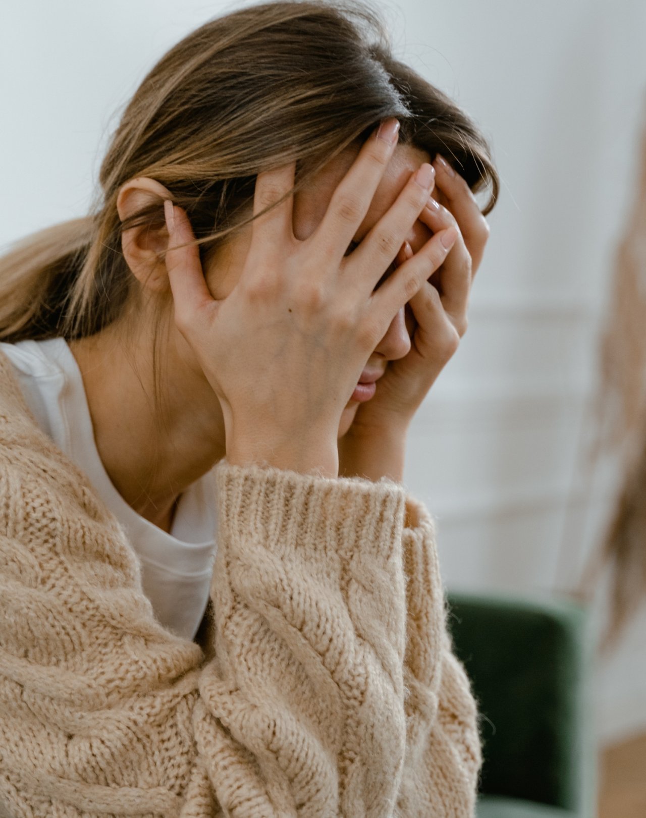 Kobieta w beżowym swetrze ukrywająca twarz w dłoniach