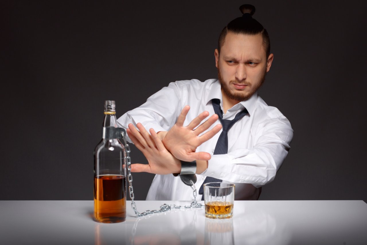Mężczyzna w rozwiązanym krawacie dramatycznym gestem odsuwa od siebie butelkę z alkoholem