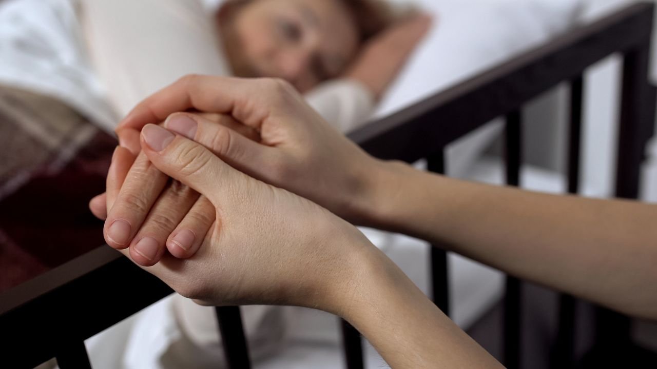 kobeita leży na łóżku, ktoś trzyma ją za dłonie