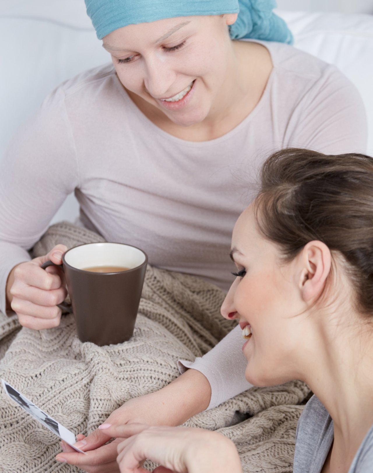 Dwie kobiety (jedna z chustą na głowie) rozmawiające ze sobą przy herbacie i fotografiach