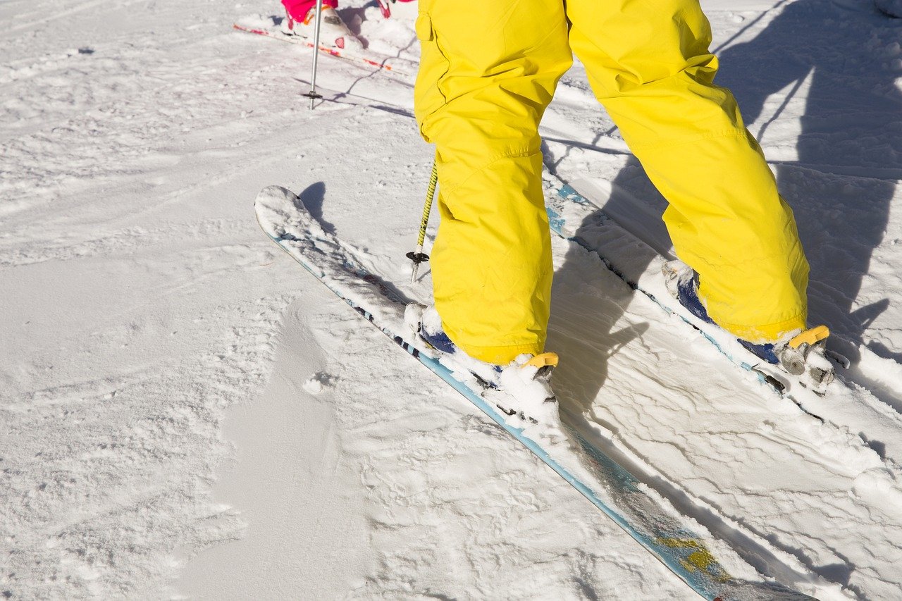 Nogi narciarza w żółtym kombinezonie w czasie jazdy na nartach na śniegu