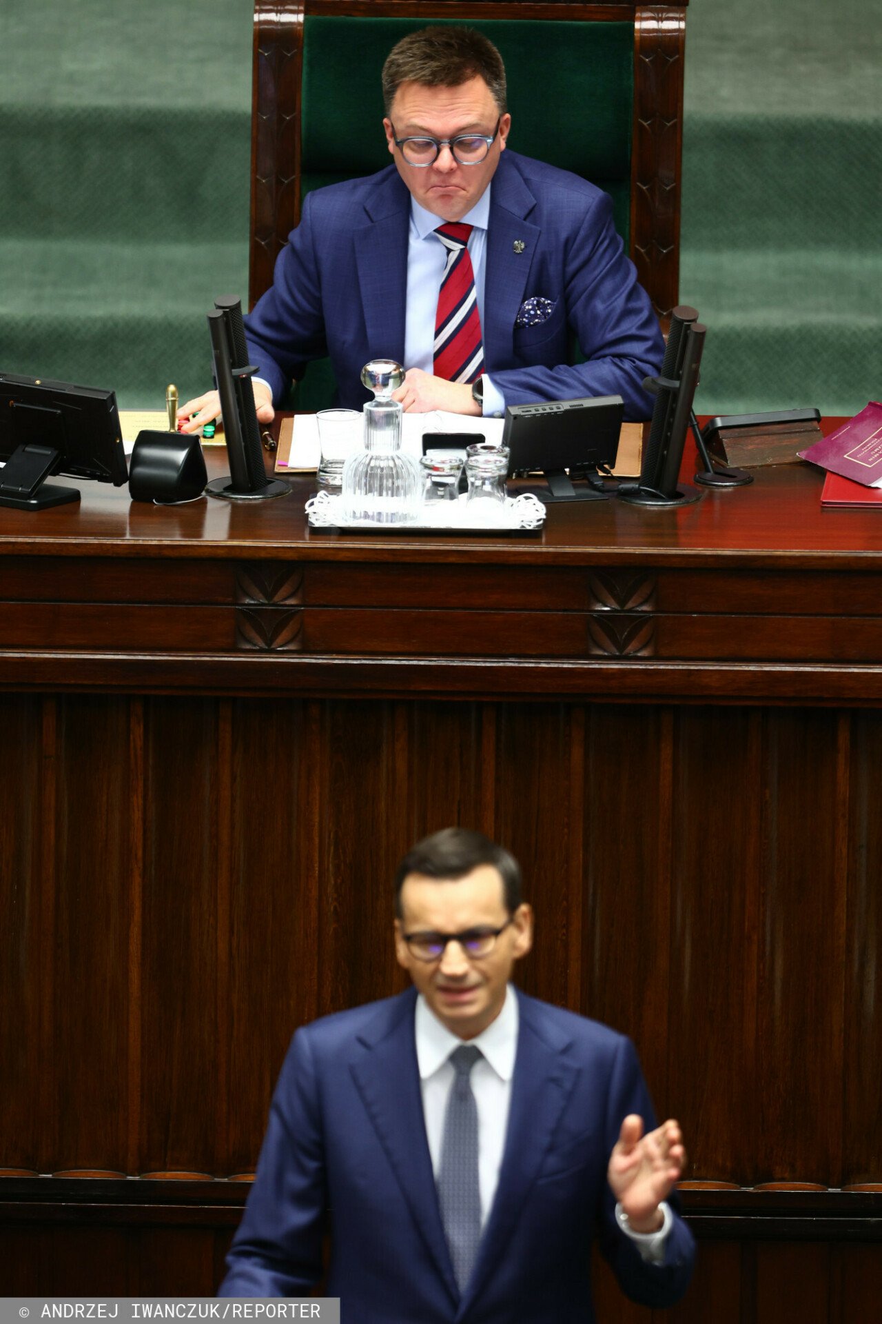 Mateusz Morawiecki z granatowym garniturze przemawia, obok Szymon Hołownia w garnatowym garniturze śmieje się