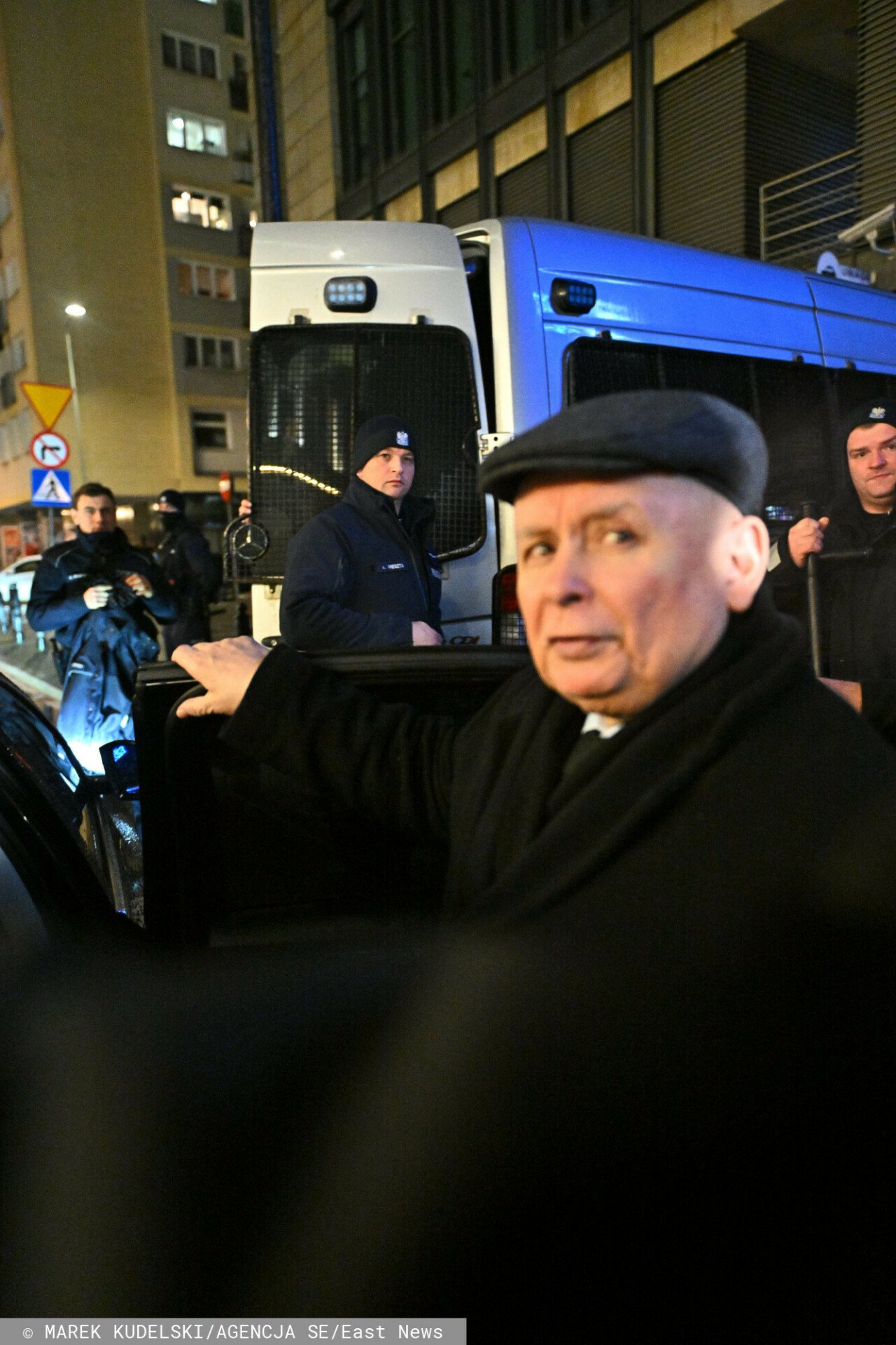 Jarosław Kaczyński przed budynkiem TVP, za nim samochód policyjny