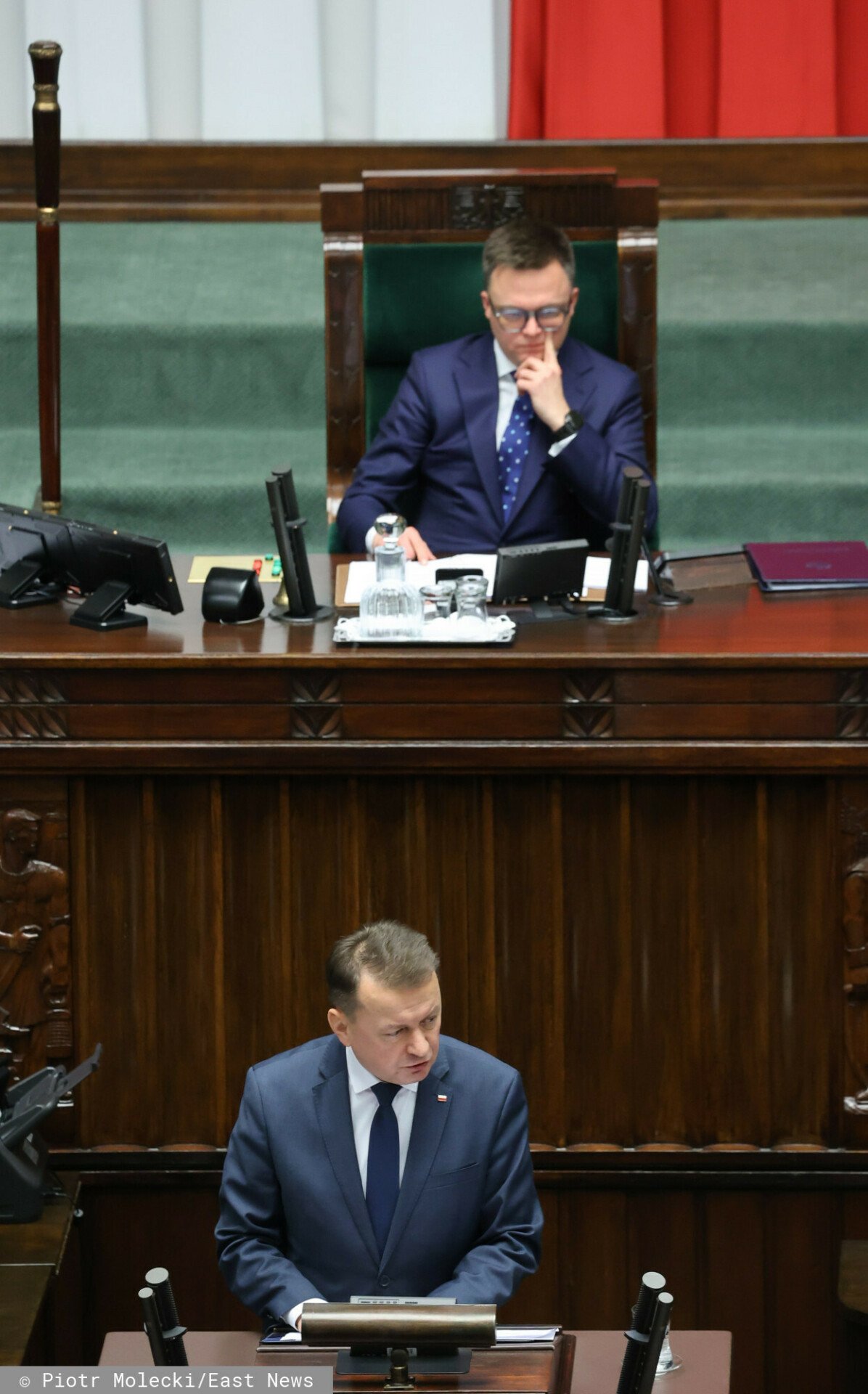 Szymon Hołownia siedzi w Sejmie, poniżej Mariusz Błaszczak przemawia