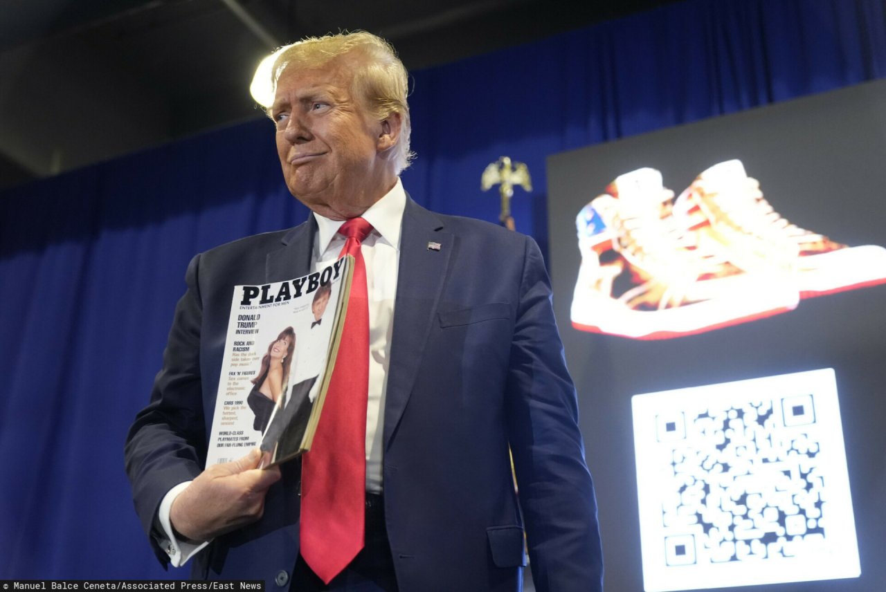 Donald Trump w granatowym garniturze trzyma złote trampki