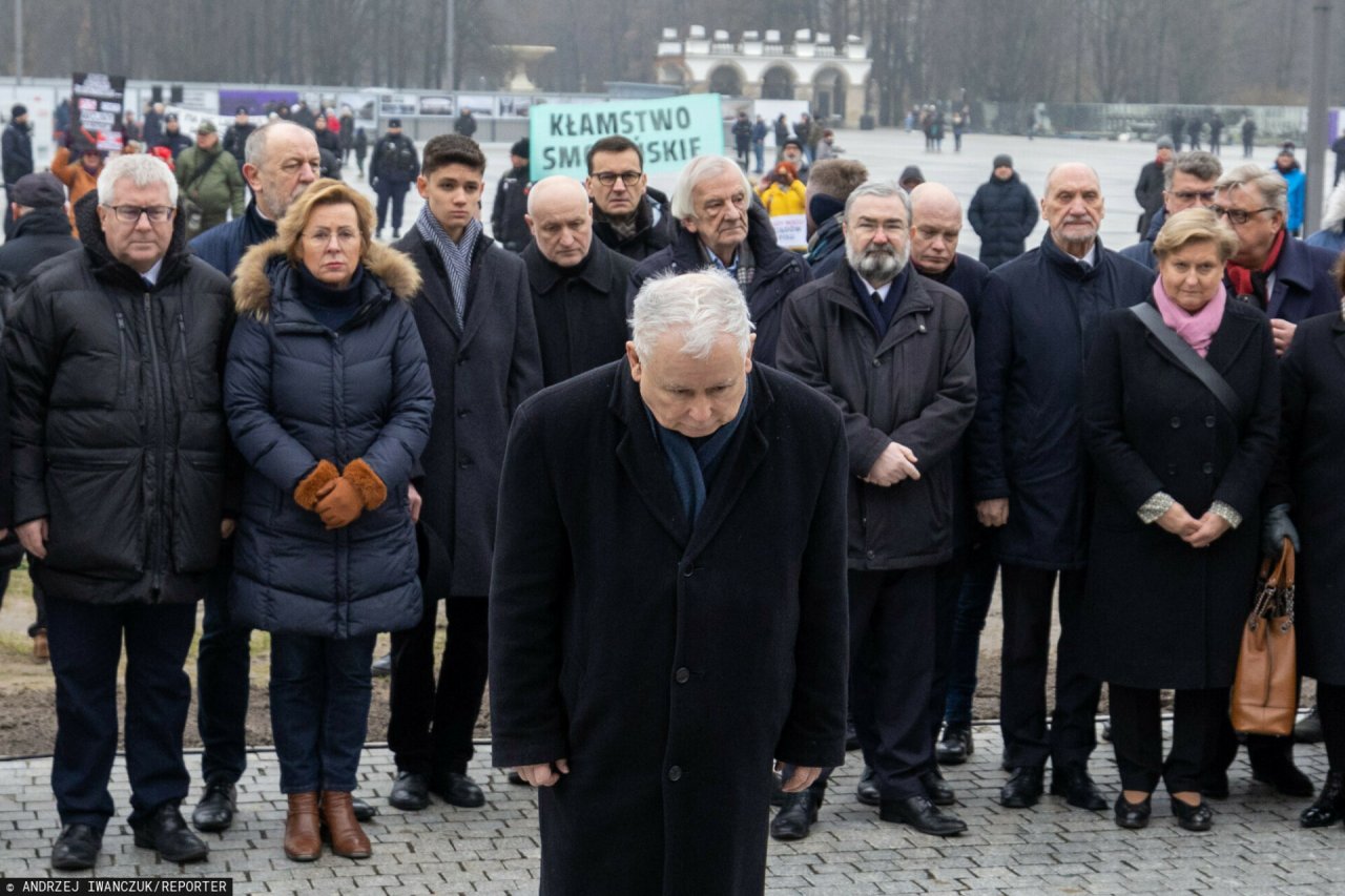Jarosław Kaczyński w czarnym płaszczu kłania się