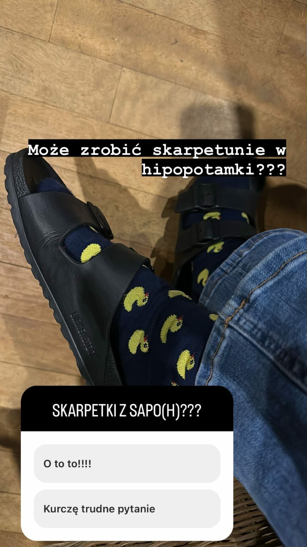 Zdjęcie z góry skarpetek w kaczki w czarnych klapkach z napisem "Może zrobić skarpetunie w hipopotamki?"
