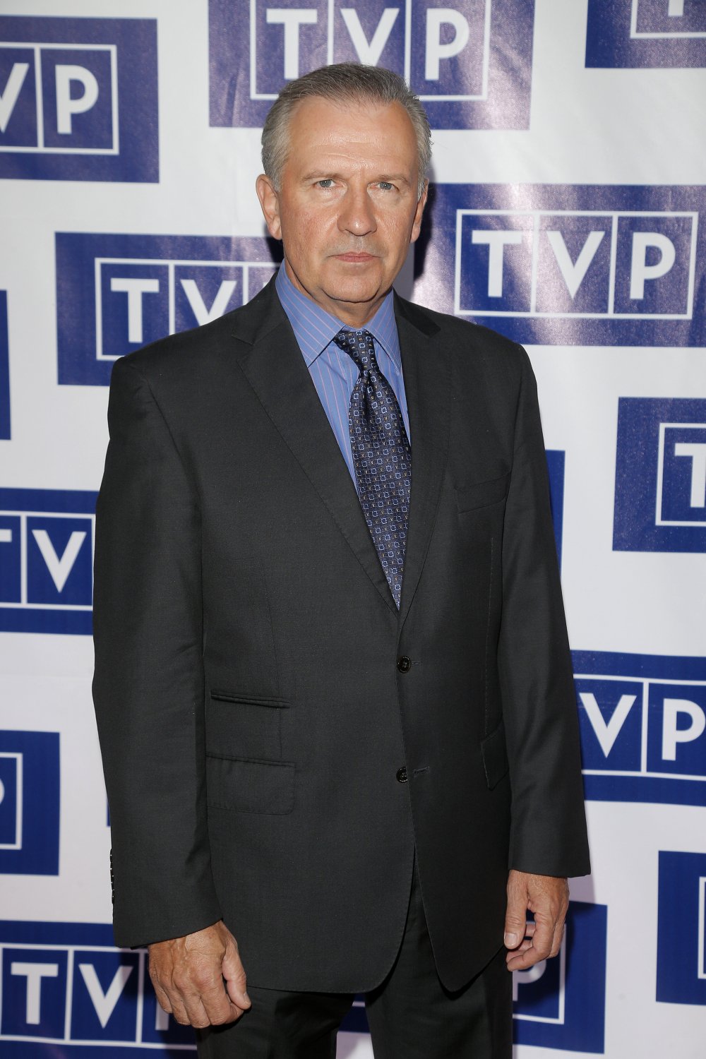 Tomasz Stockinger w garniturze i niebieskiej koszuli na ściance TVP