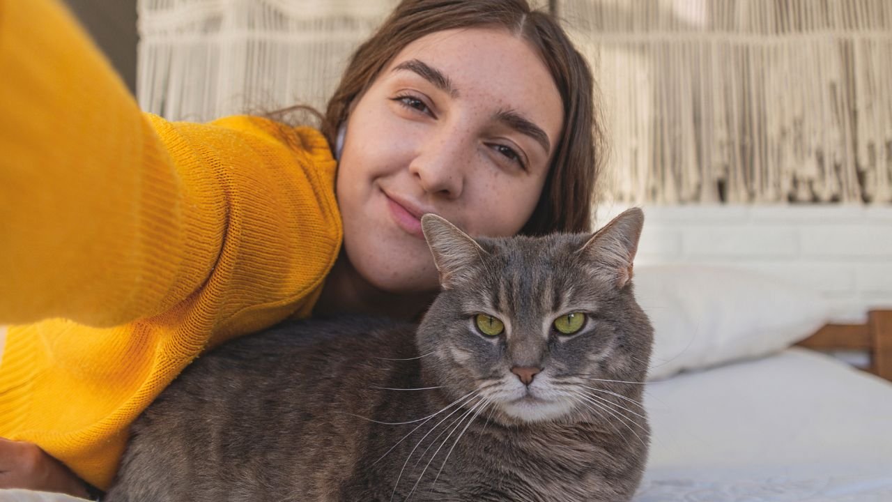 młoda kobieta w pomarańczowym swetrze przytula kota