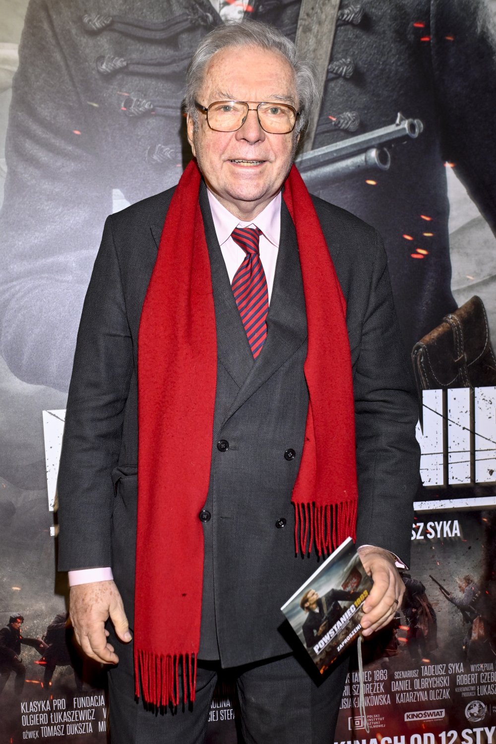 Krzysztof Zanussi w garniturze, czerwonym krawacie i czerwonym szaliku