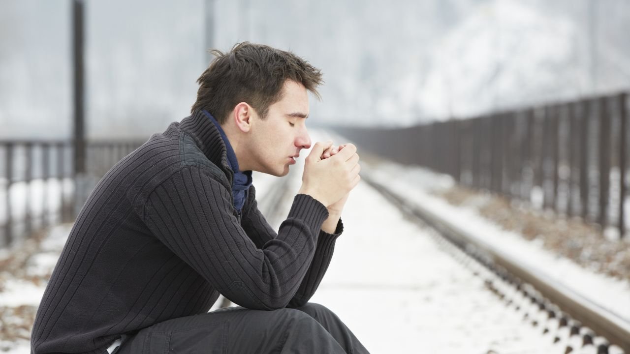 mężczynza siedzi na śniegu i chucha w dłonie