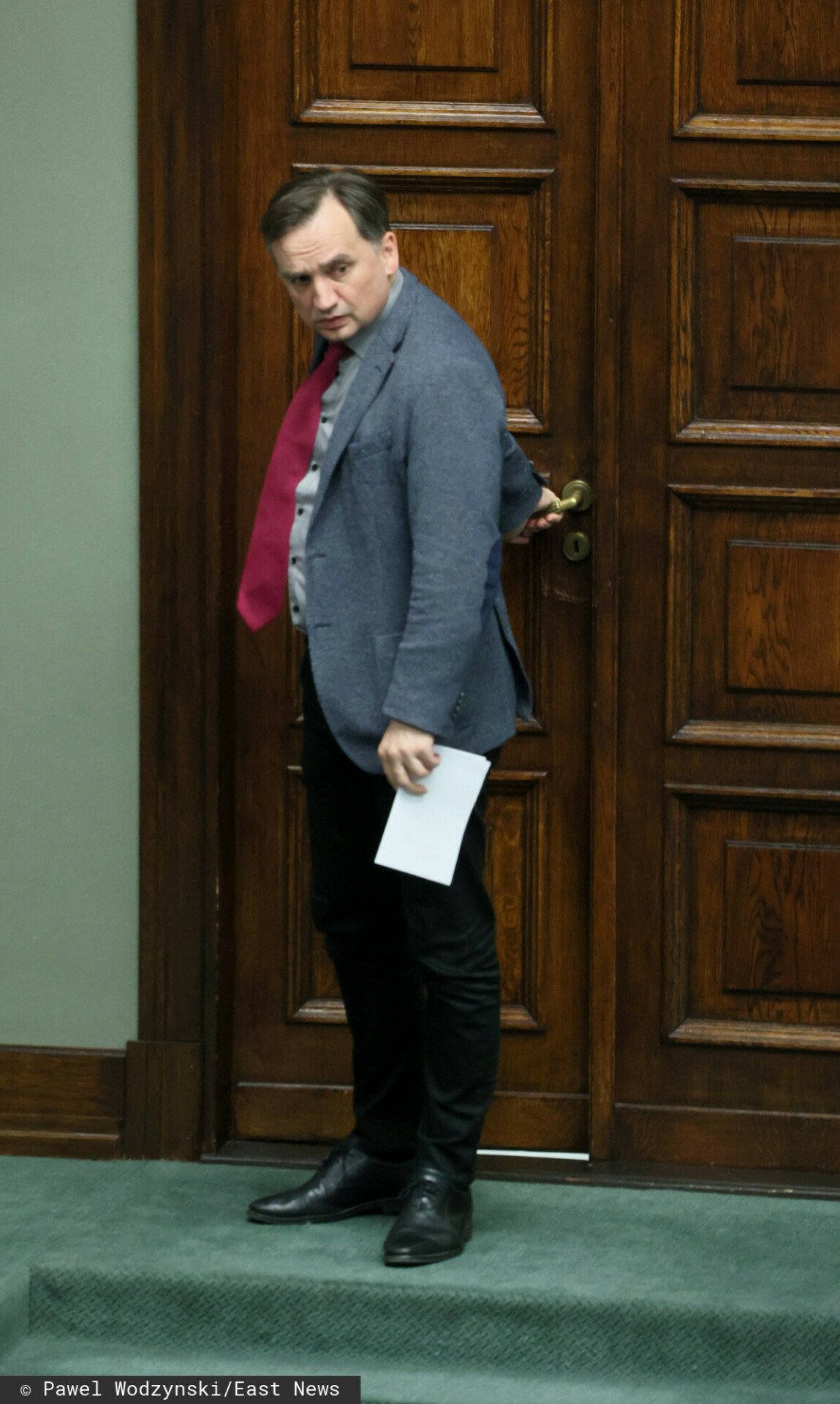 Zbigniew Ziobro w szarej marynarce i czerwonym krawacie zamykający drzwi w Sejmie RP