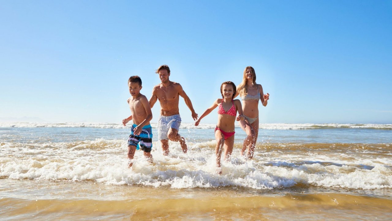 Rodzice z dwójką dzieci radośnie wybiegają z morza na plażę