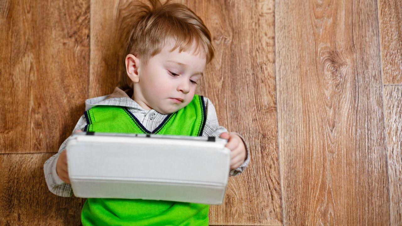 Mały chłopiec leży na podłodze i trzyma tablet.
