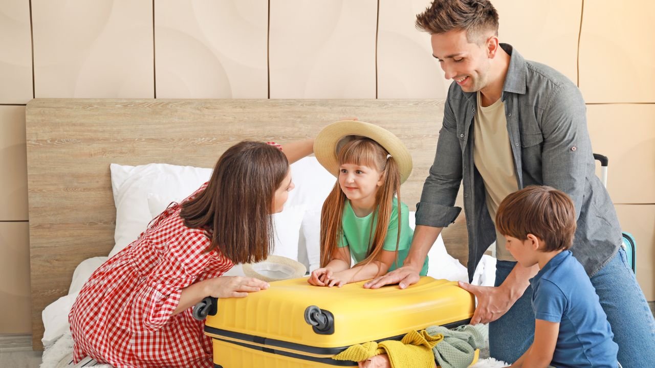 rodzina z dziećmi pakująca na łóżku żółtą walizkę 